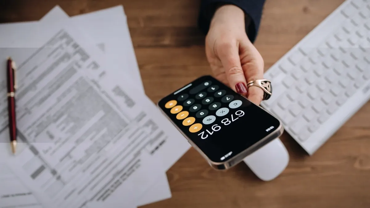 Hand hält Smartphone mit Taschenrechner über Unterlagen als Symbol für die Berechnung einer Mieterhöhung